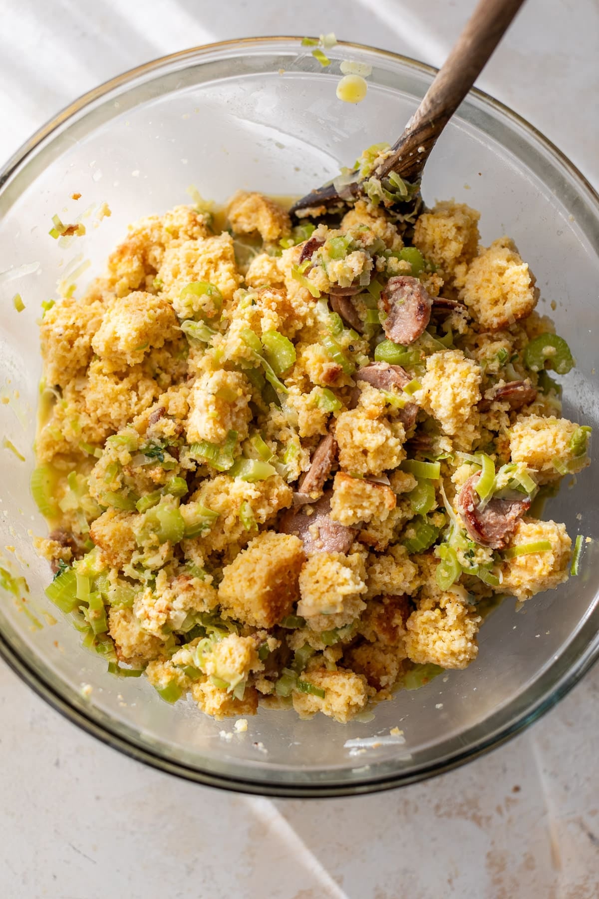 using a wooden spoon to stir Chicken Sausage Cornbread Stuffing in a glass bowl.