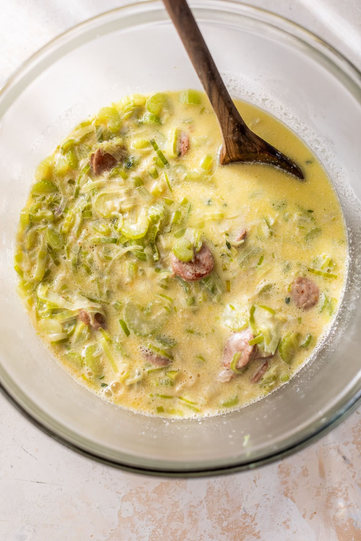 using a wooden spoon to stir the liquid mixture for Chicken Sausage Cornbread Stuffing in a glass bowl.