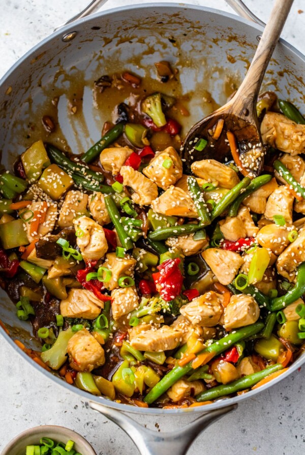a skillet filled with cooked chicken and vegetables coated in a sauce and topped with sesame seeds