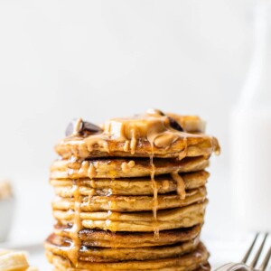 stack of pancakes on a plate with peanut butter and maple syrup