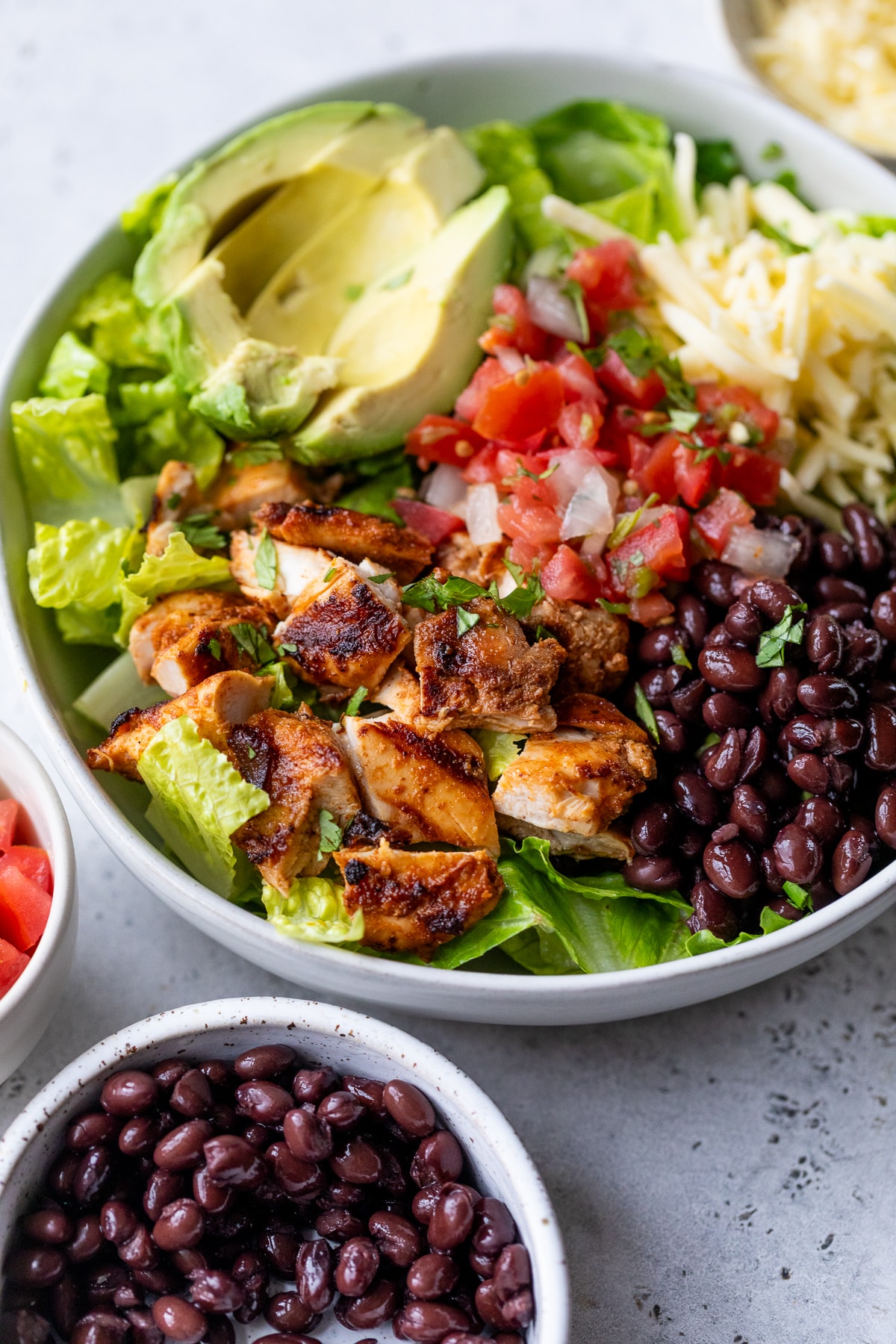 a burrito bowl topped with grilled chipotle chicken, black beans, salsa, cheese, and avocado.
