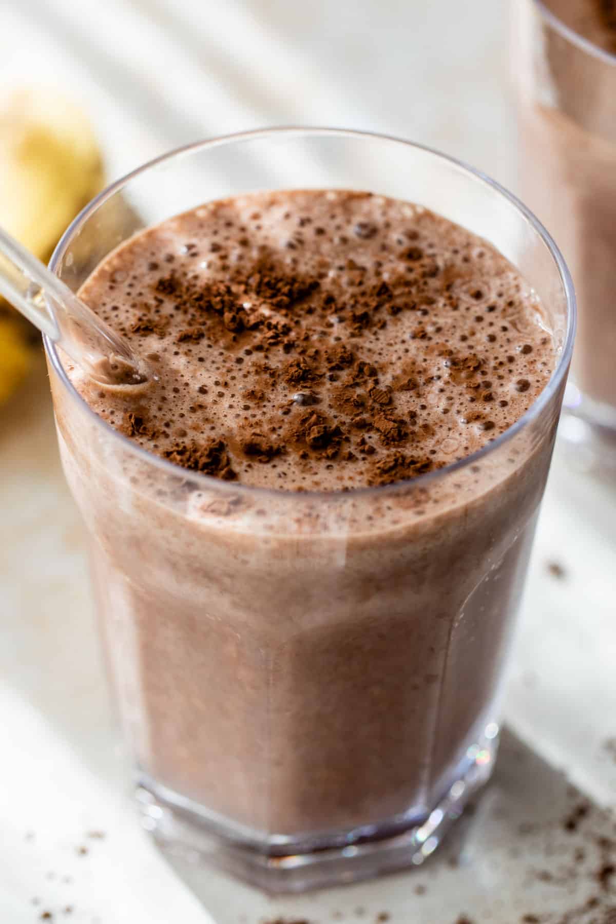 close-up of a chocolate banana smoothie in a glass with a straw and cocoa powder sprinkled on top