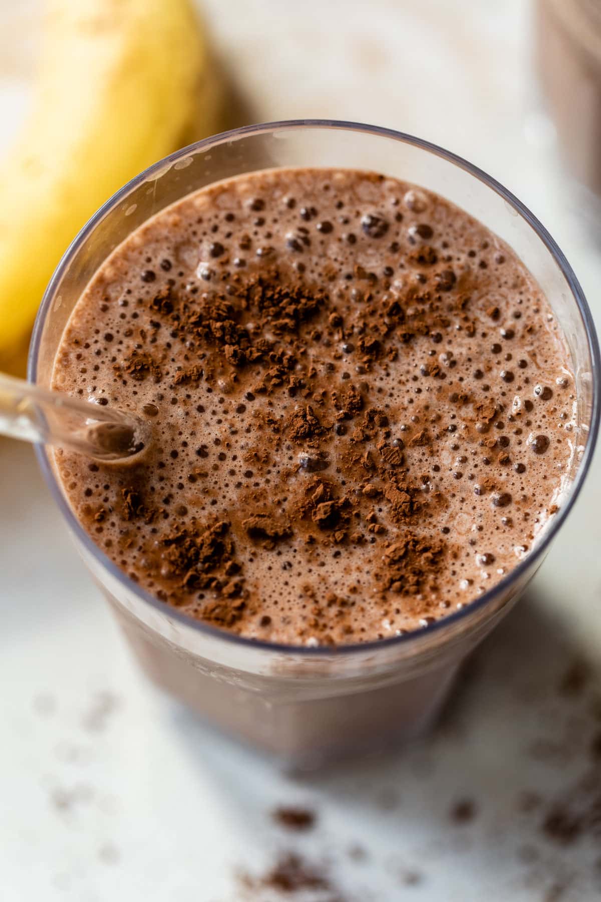 overview of a chocolate banana smoothie in a glass with a straw and cocoa powder sprinkled on top