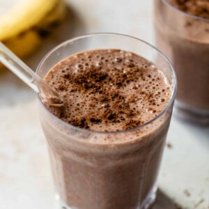 chocolate banana smoothie in a glass with a straw and cocoa powder sprinkled on top