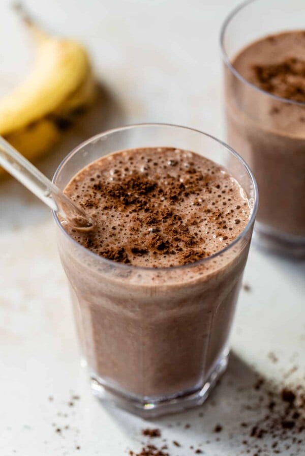 chocolate banana smoothie in a glass with a straw and cocoa powder sprinkled on top