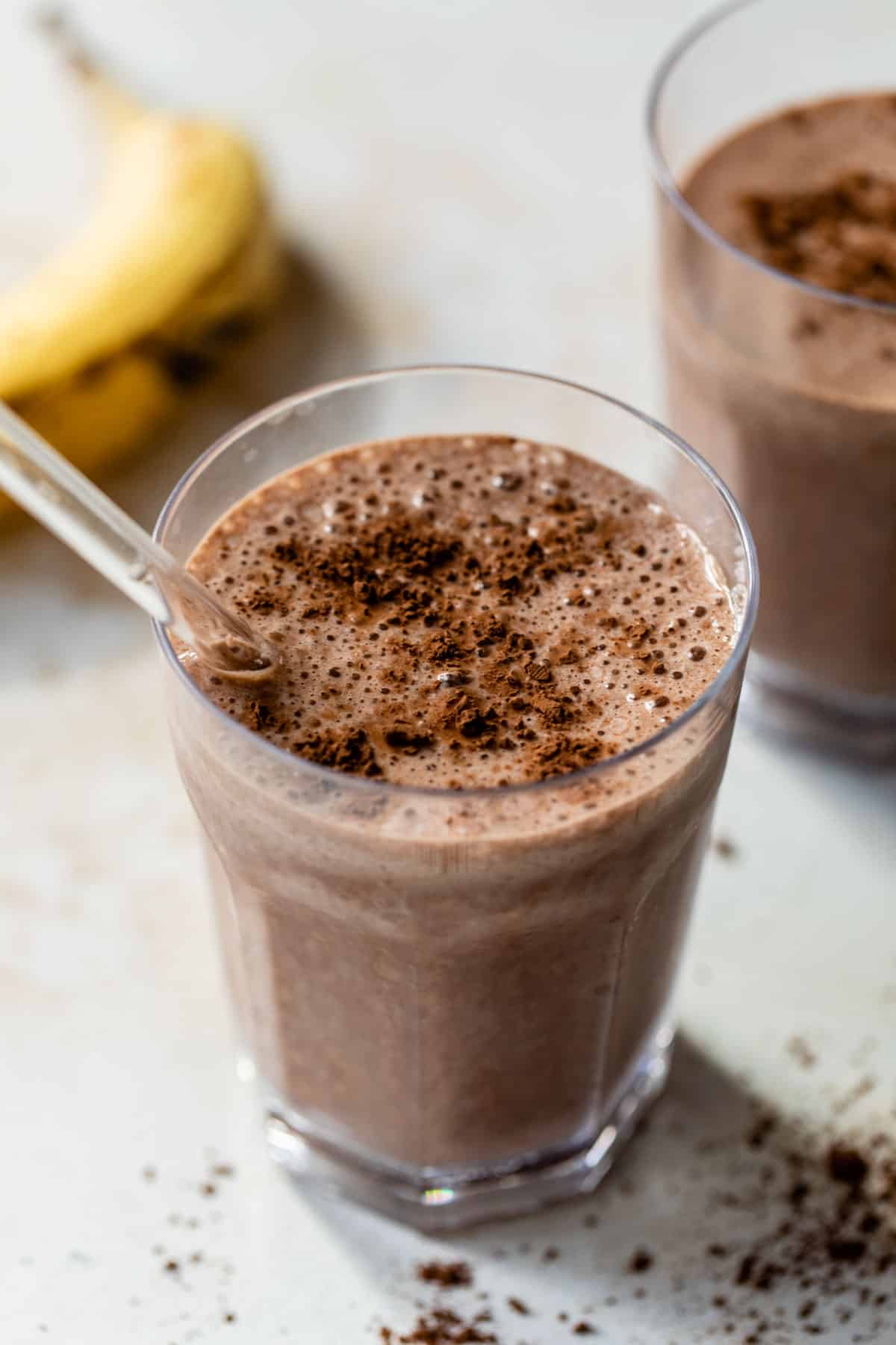 chocolate banana smoothie in a glass with a straw and cocoa powder sprinkled on top