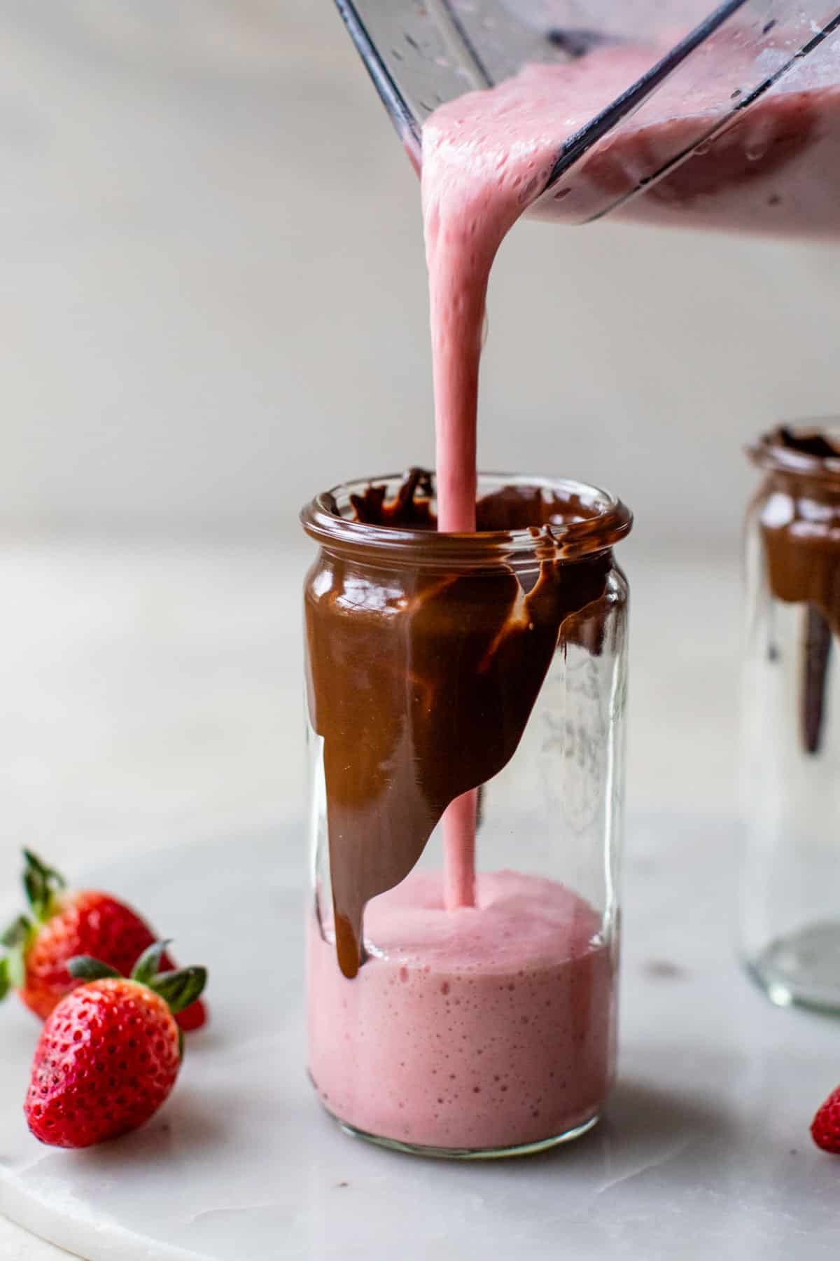 someone pouring a pink smoothie from a blender into a glass