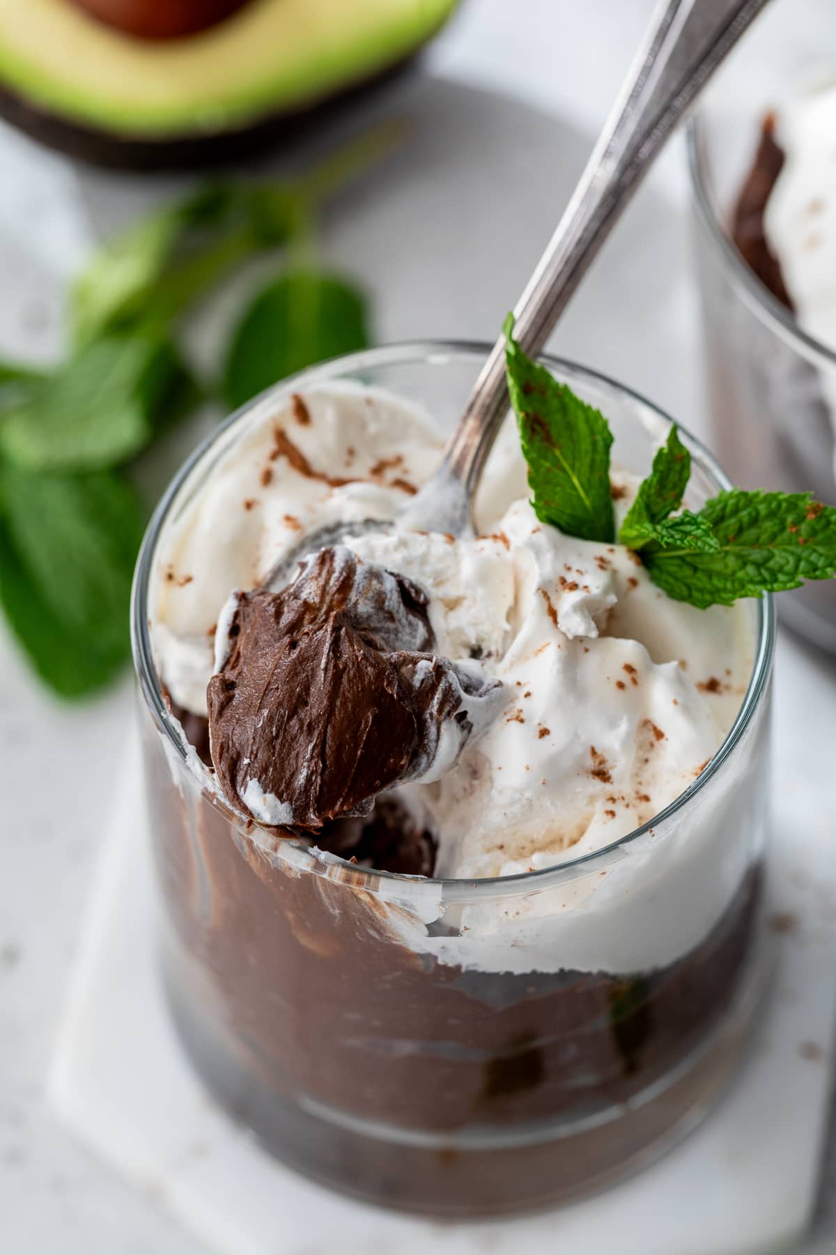 a spoon lifting a scoop of chocolate avocado pudding from a glass container.