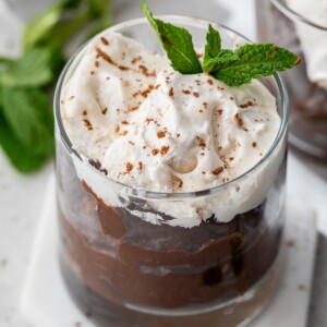 chocolate avocado pudding topped with whipped cream in a glass container.