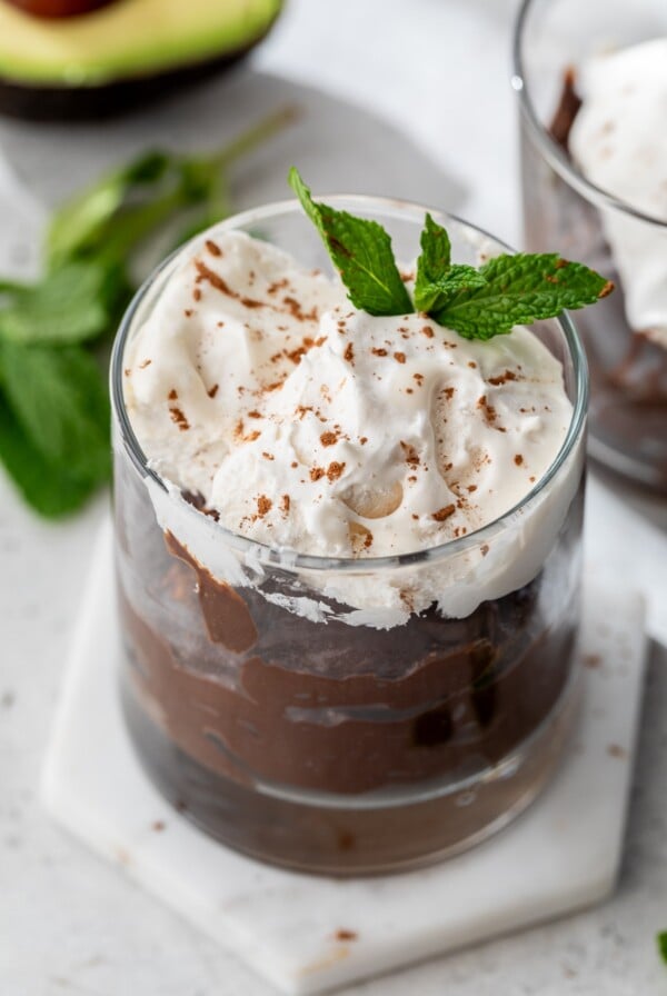 chocolate avocado pudding topped with whipped cream in a glass container.