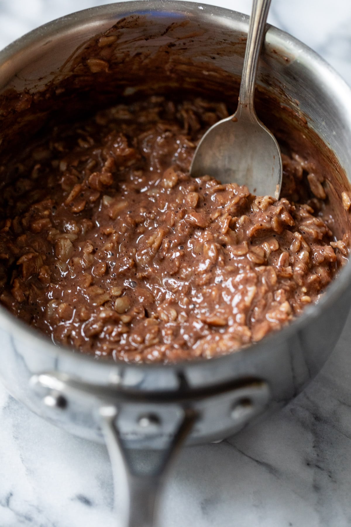using a spoon to stir chocolate oatmeal in a saucepan.