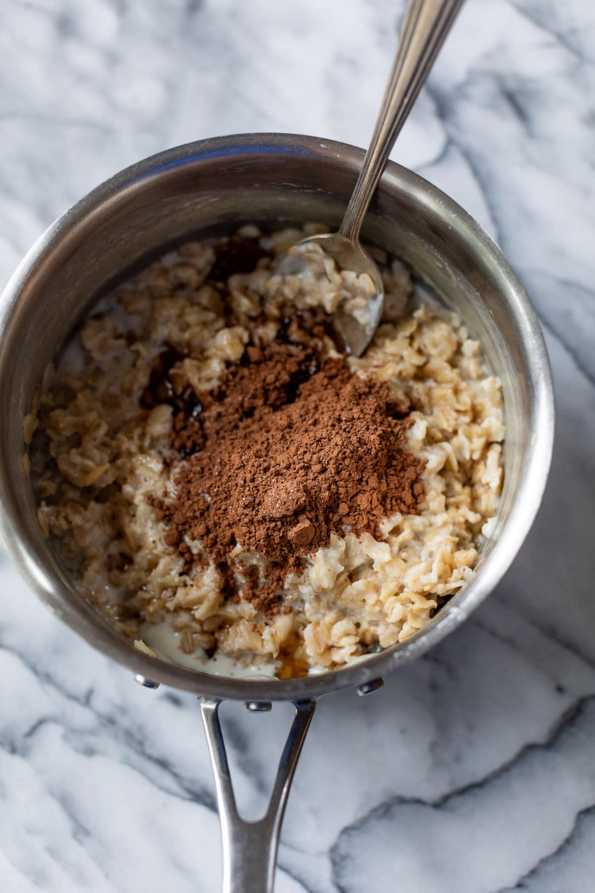 using a spoon to stir cocoa powder into a pot of cooked oats.
