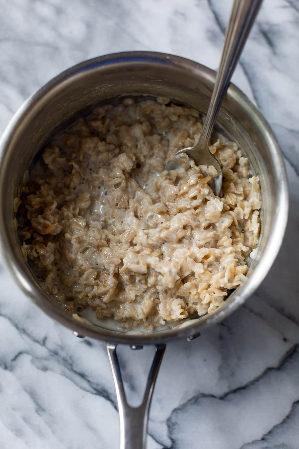 using a spoon to stir cooked oats in a pot.