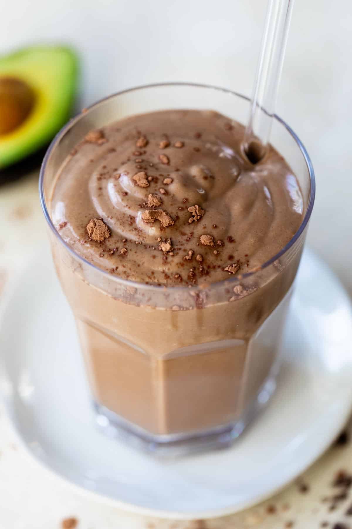 chocolate smoothie in a glass with a straw beside an avocado