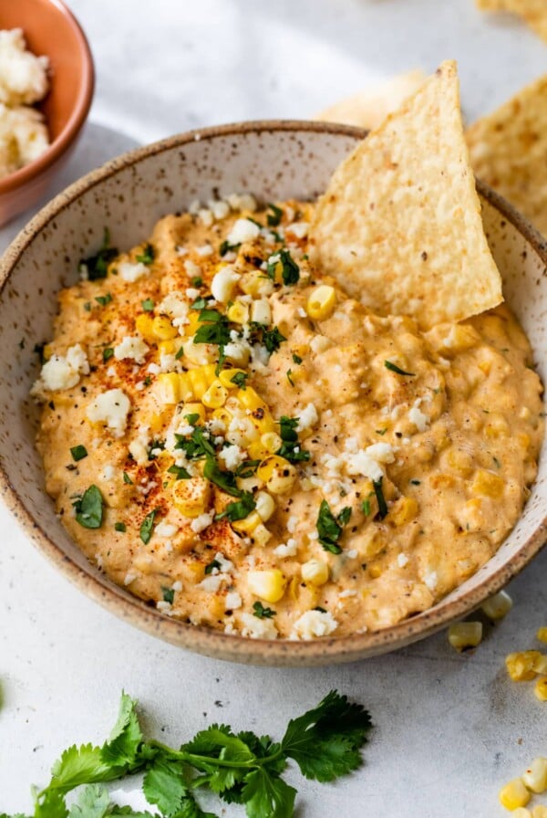 corn dip in a bowl with a chip topped with chopped cilantro and cotija cheese