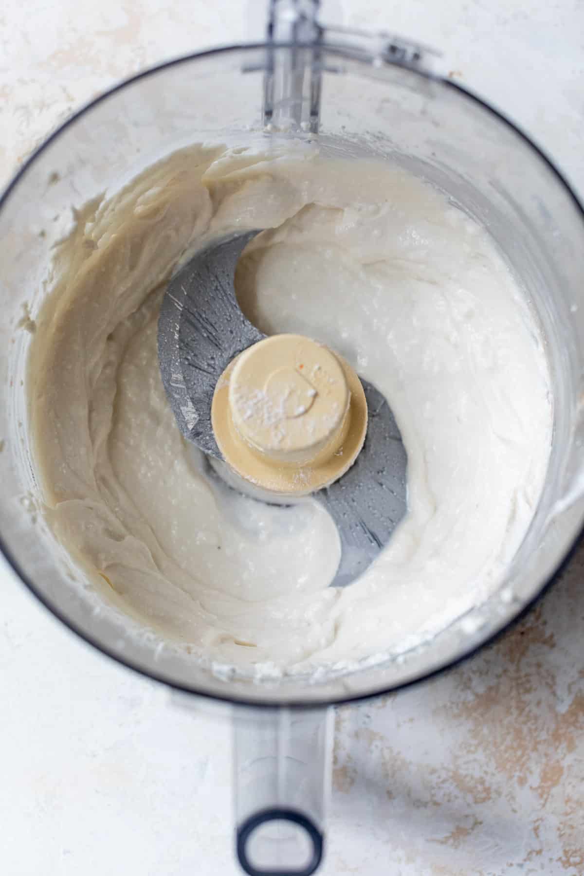 overhead view of a creamy white mixture in a food processor.