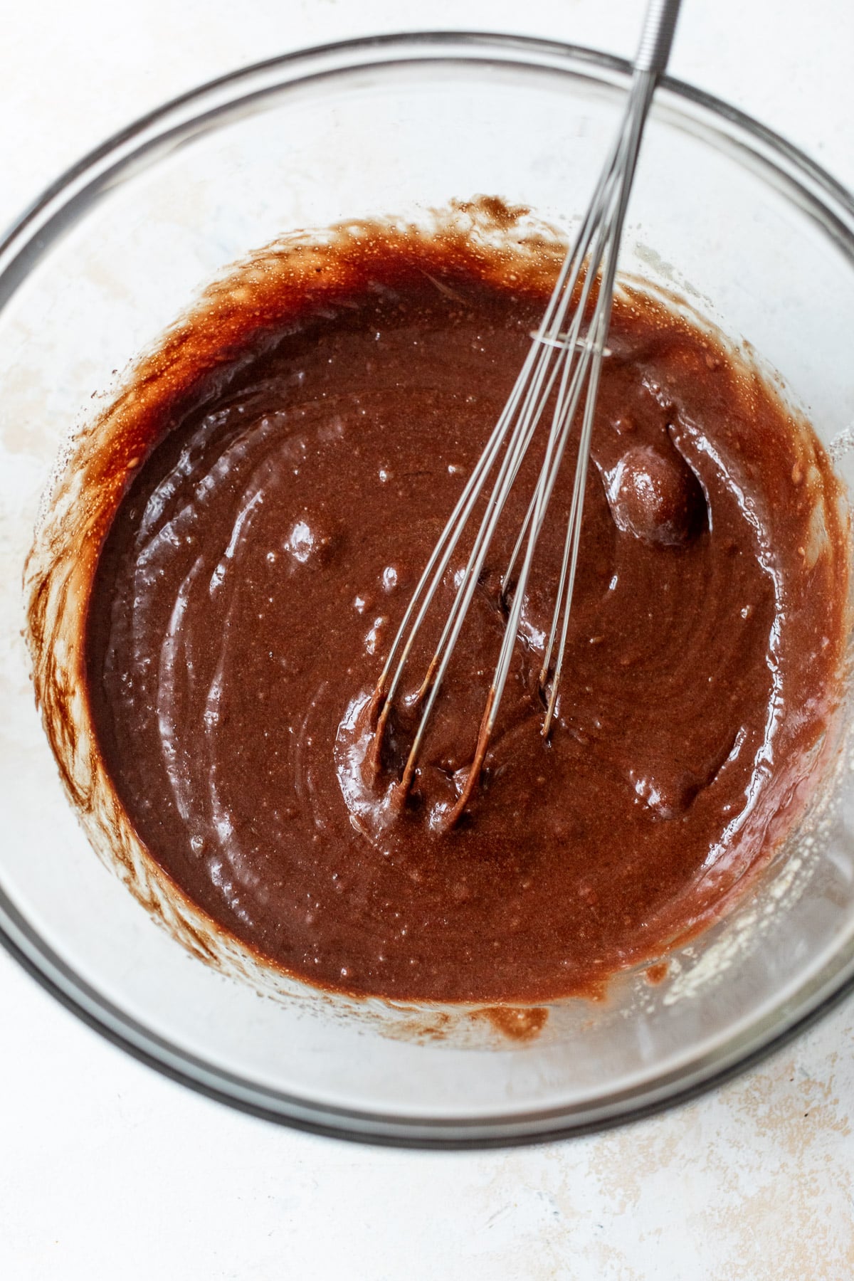 overhead view of a whisk in a liquid chocolate brownie batter in a glass bowl.