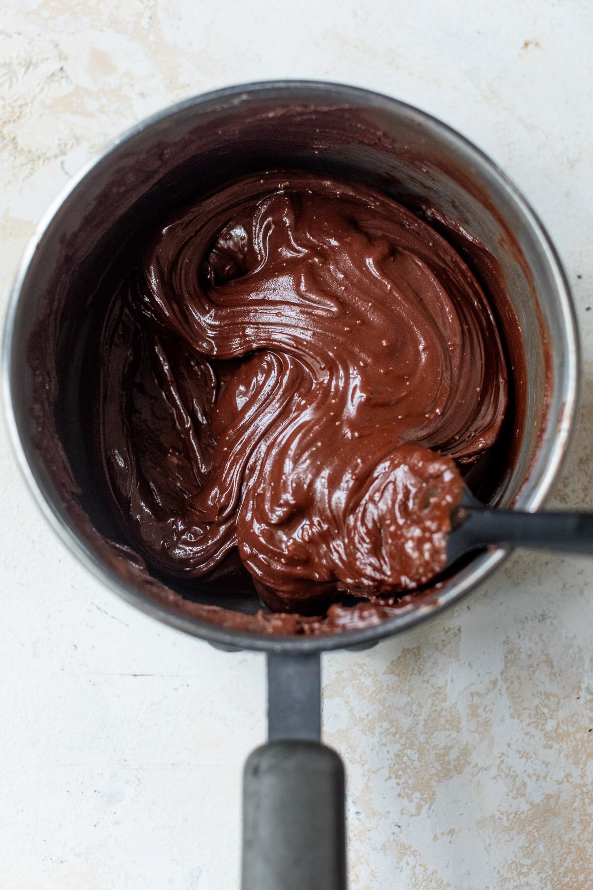 overhead view of melted chocolate and a black spatula in a saucepan.