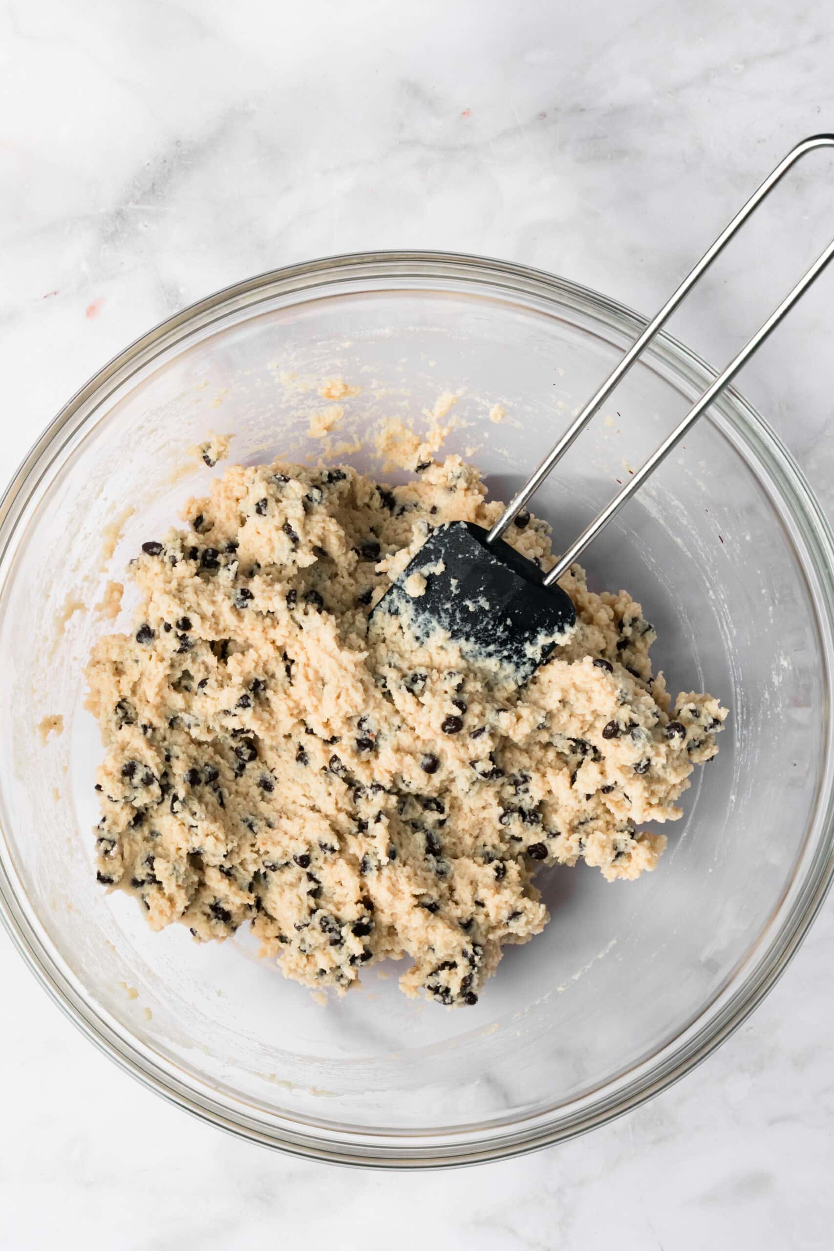 overhead view of a black spatula mixing chocolate chip cottage cheese cookie dough in a glass bowl.