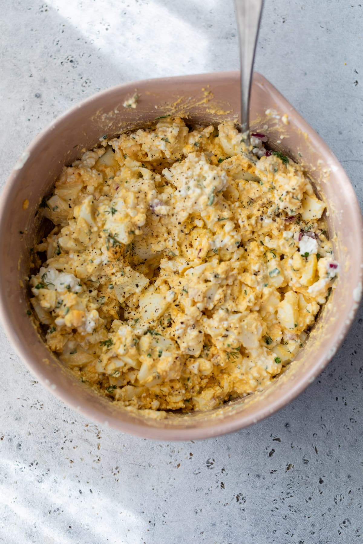 using a spoon to stir cottage cheese egg salad in a large pink bowl.