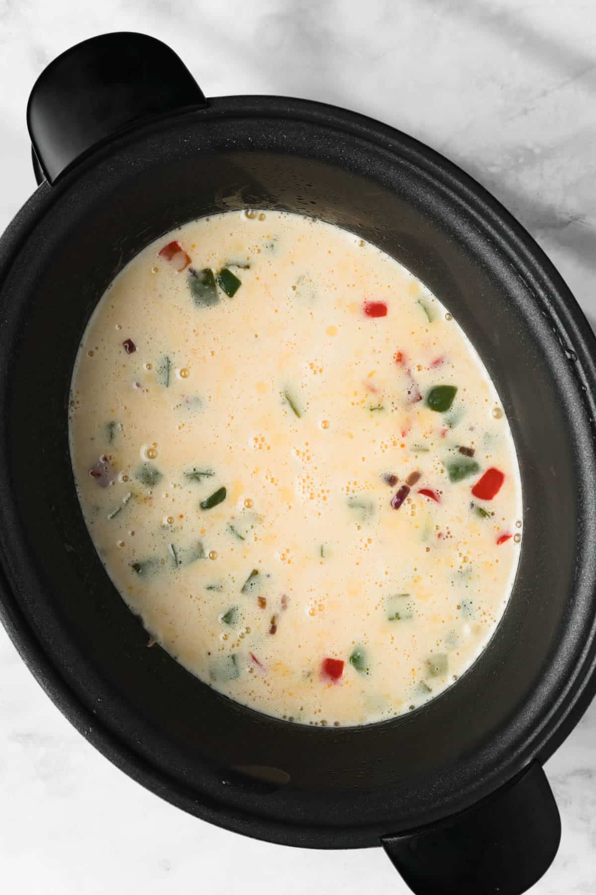 overhead view of a liquid egg mixture in a crockpot with vegetables for a crockpot breakfast casserole.