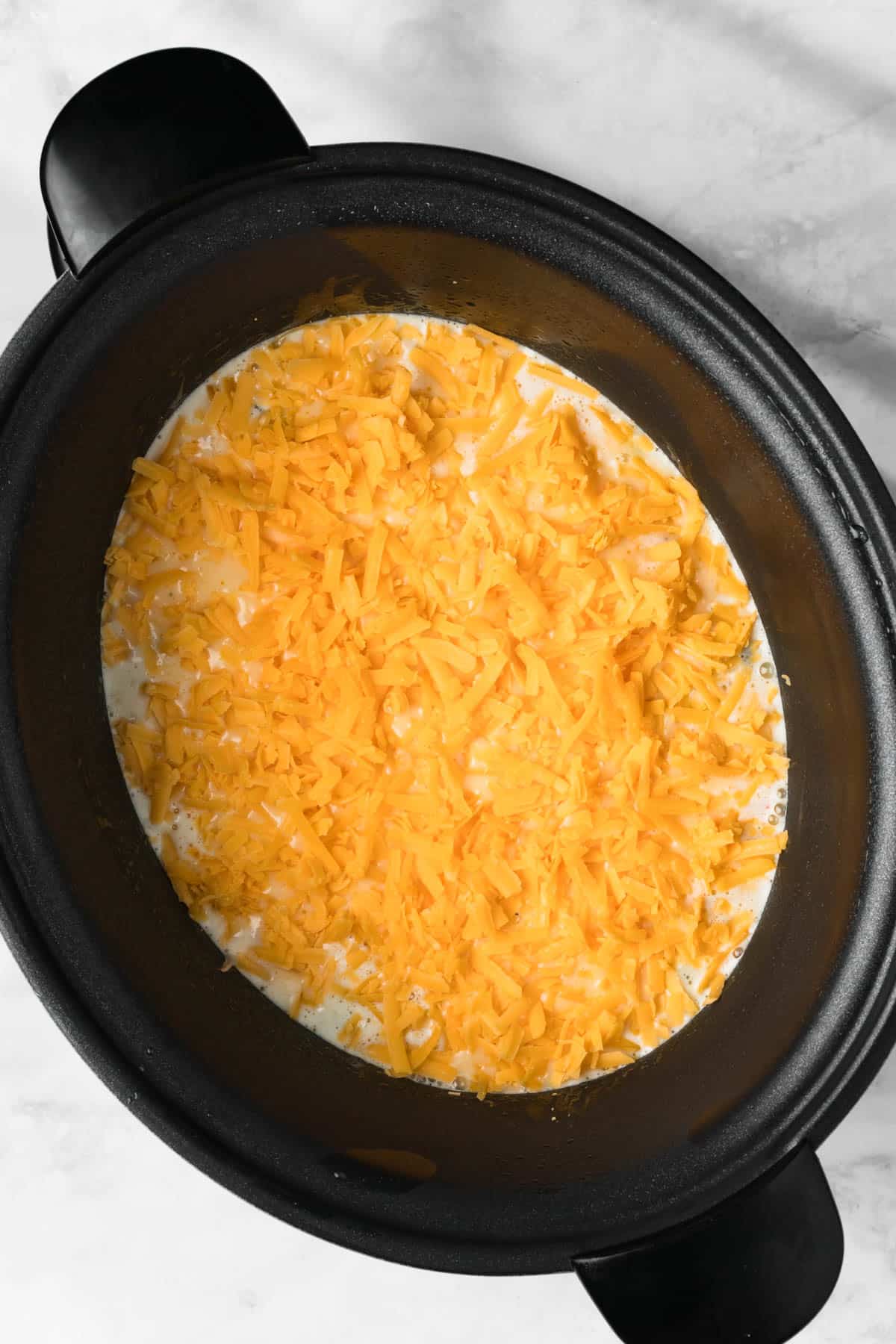overhead view of shredded cheese on top of liquid eggs in a crockpot for a crockpot breakfast casserole.