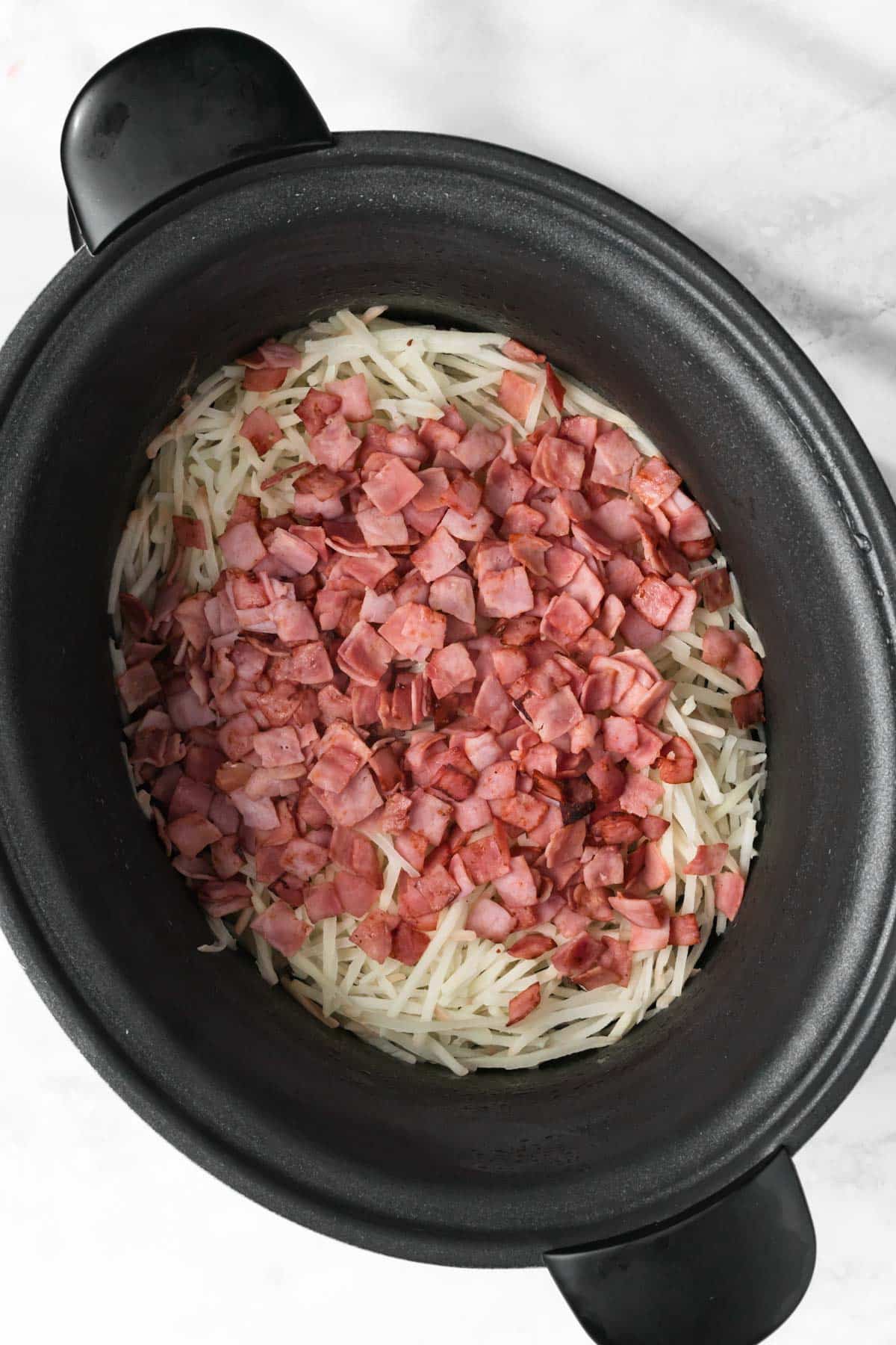 overhead view of cooked bacon on top of hashbrowns in a crockpot.