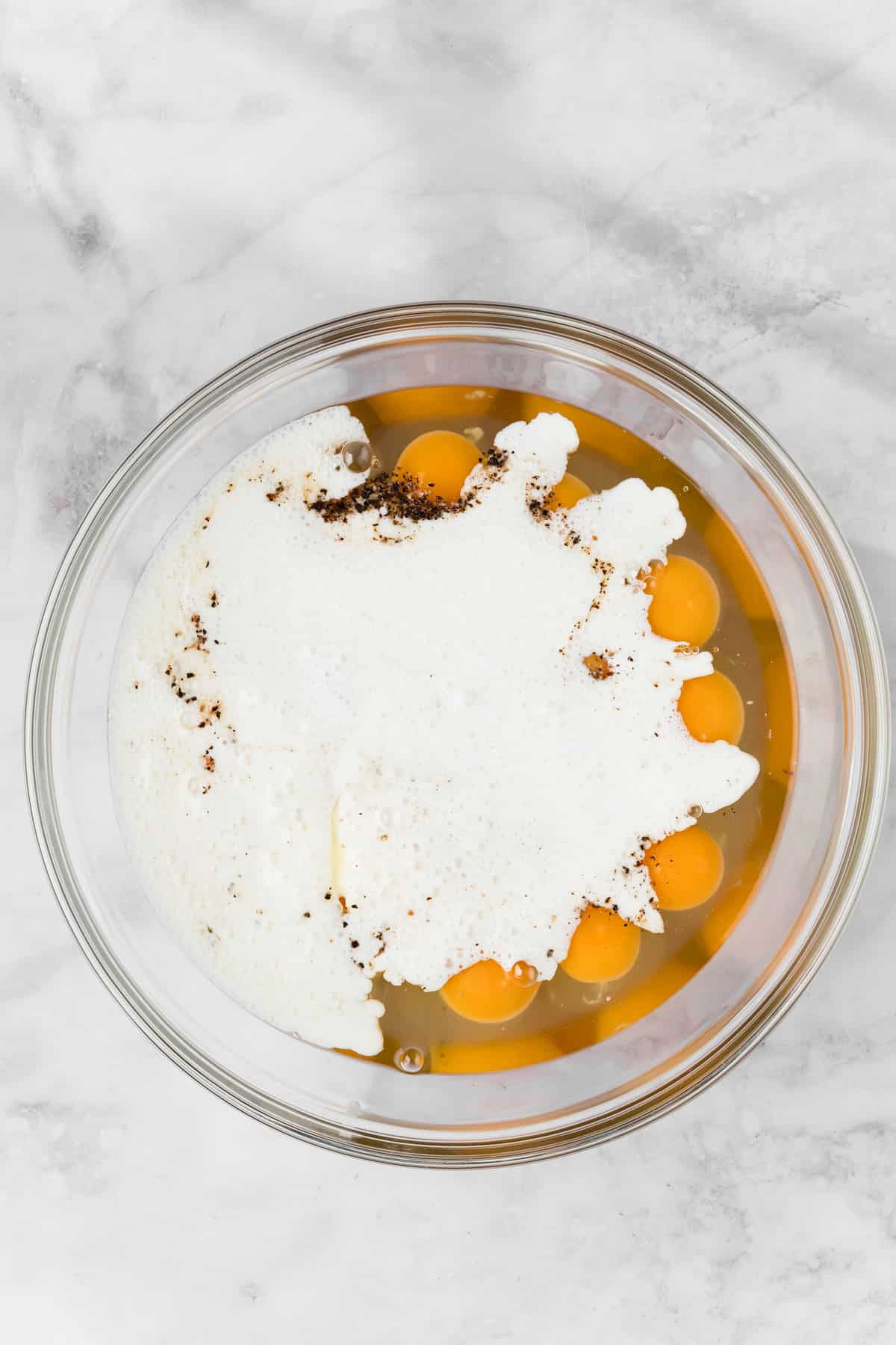 overhead view of egg yolks and milk in a large glass bowl for a crockpot breakfast casserole.