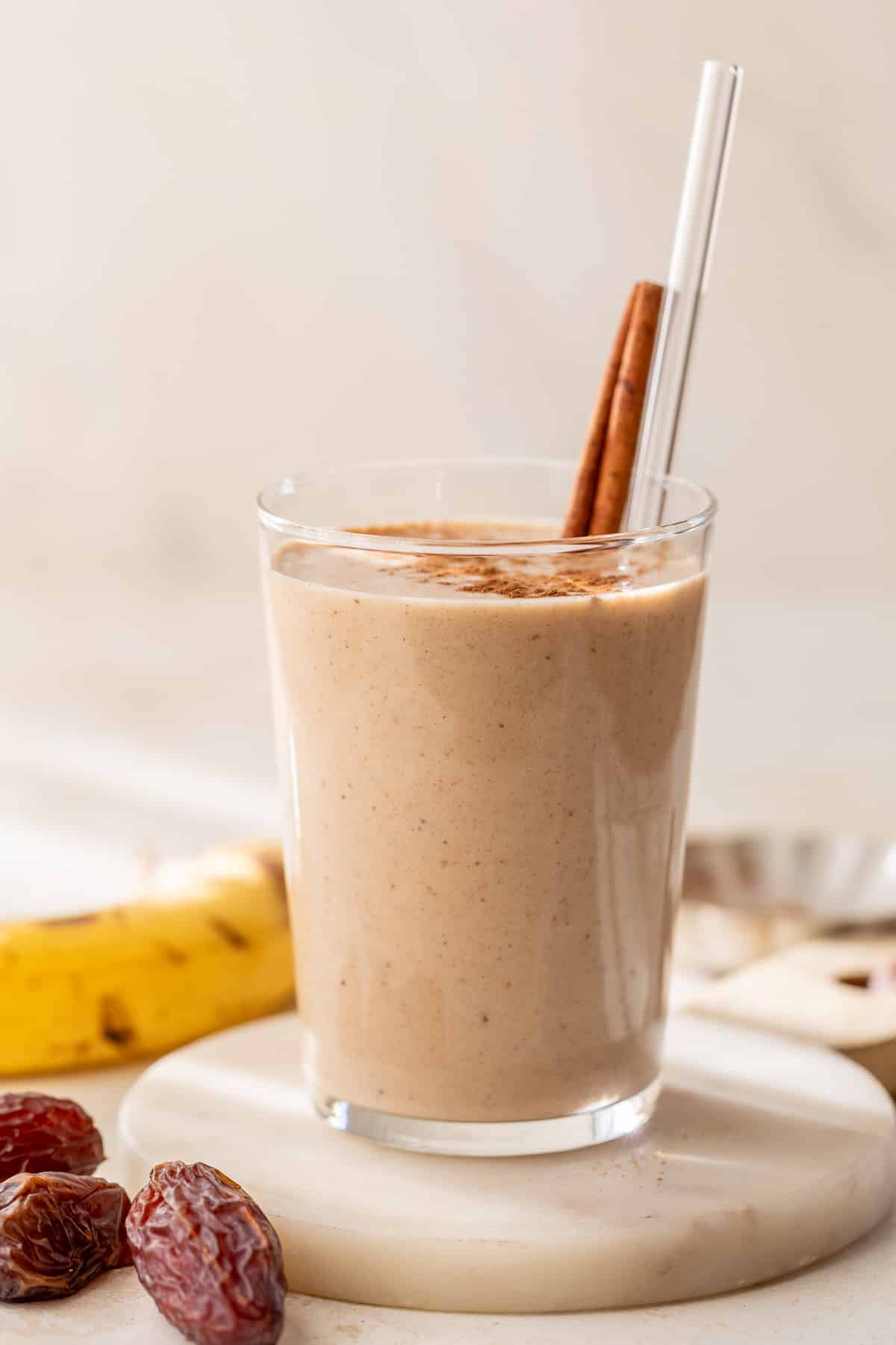 side view of a date smoothie in a glass with a straw and cinnamon stick