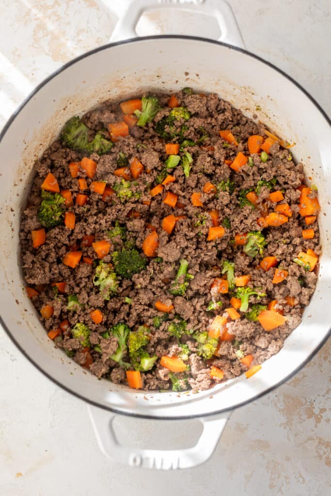 cooked ground beef, carrots and broccoli in a white dutch oven