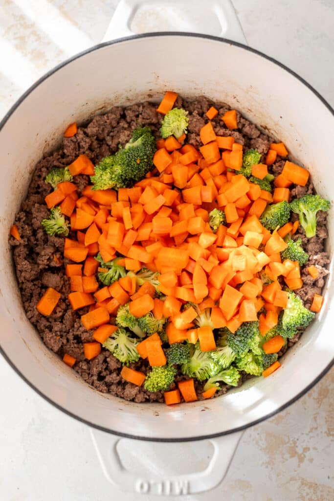 cooked ground beef, uncooked diced carrots and chopped broccoli in a white dutch oven