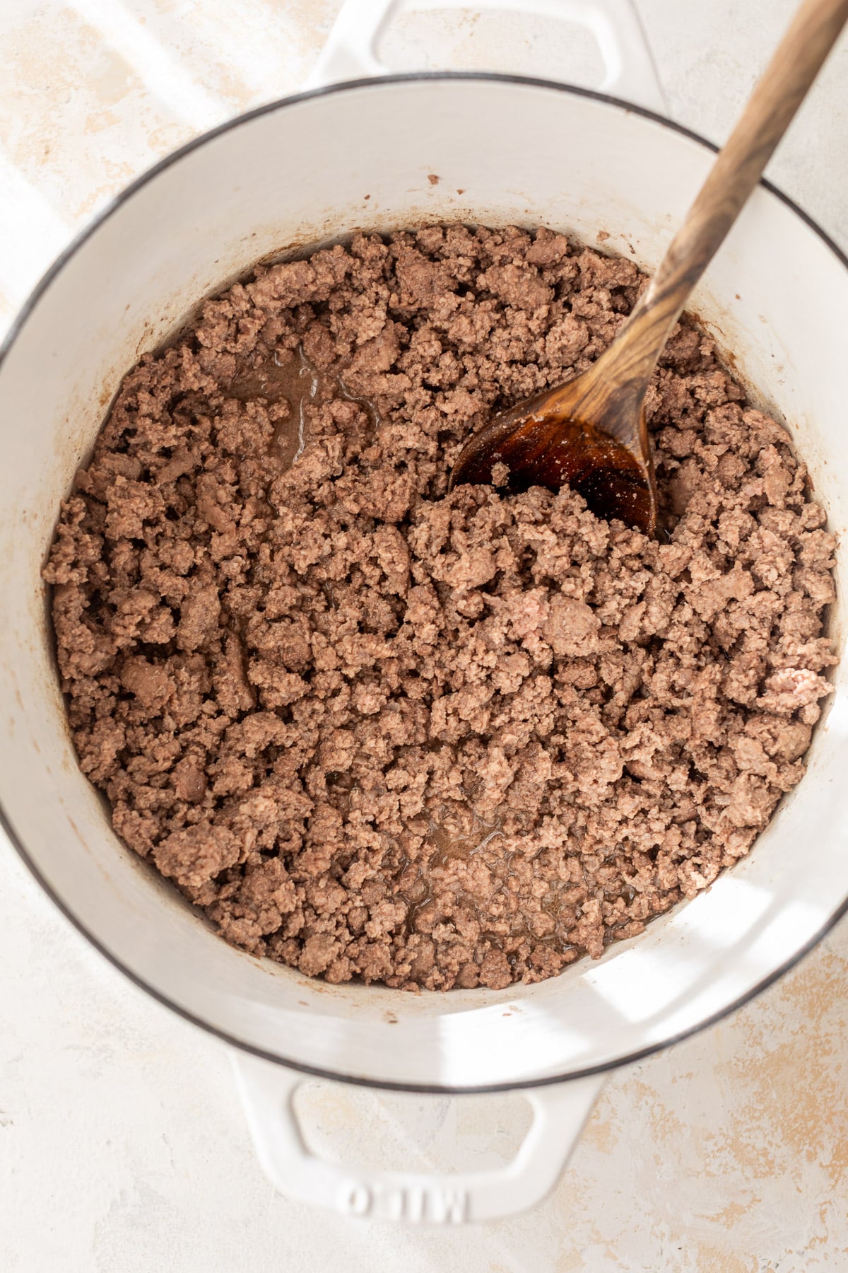 cooked ground beef in a white dutch oven with a wooden spoon