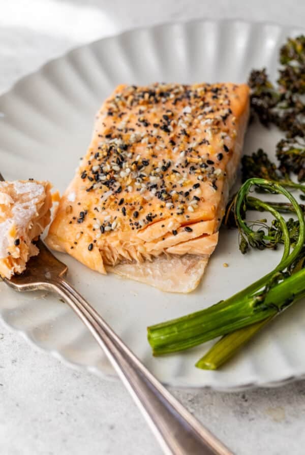 close up on a fork taking a bite out of an everything bagel salmon filet on a white plate.