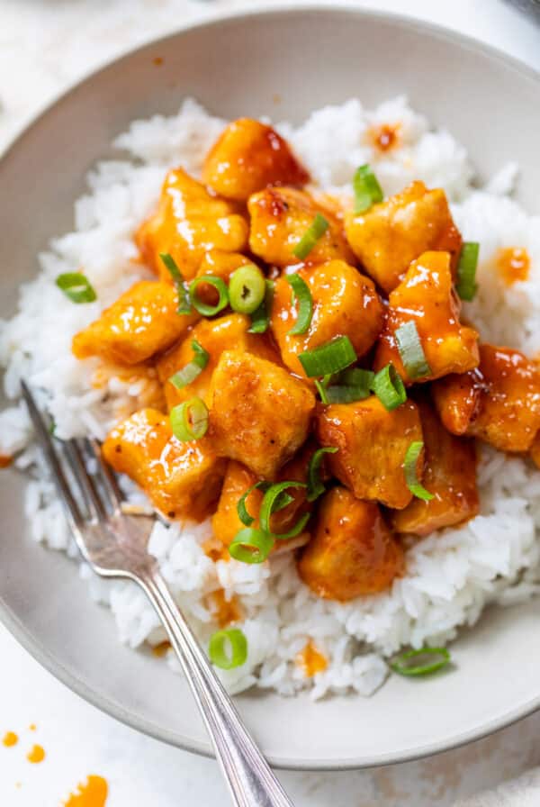 a scoop of saucy orange firecracker chicken served over white rice in a bowl.