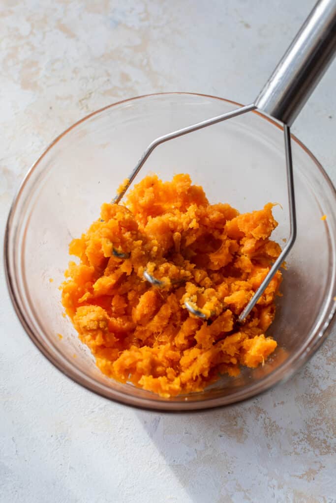 mashed sweet potato in a bowl with a potato masher