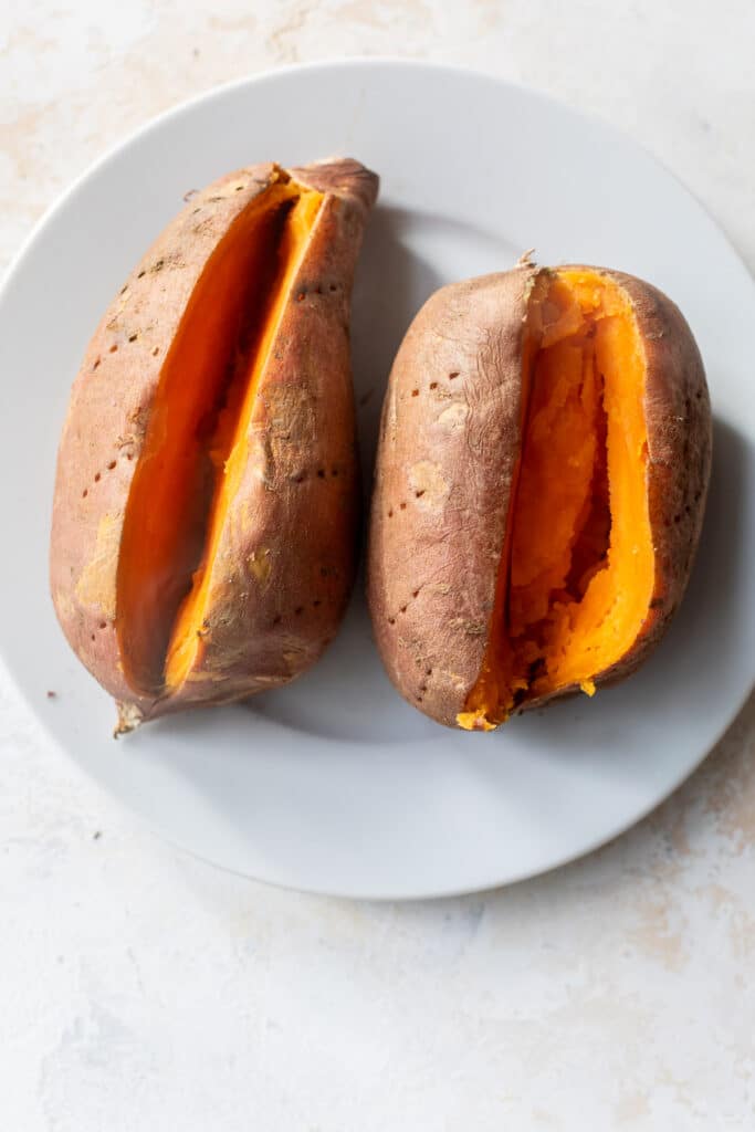 two cooked sweet potatoes sliced down the middle on a white plate