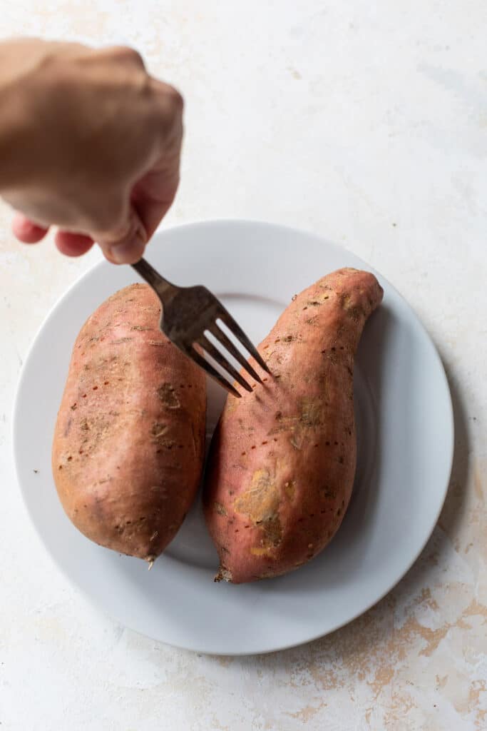 someone poking holes in two sweet potatoes on a white plate