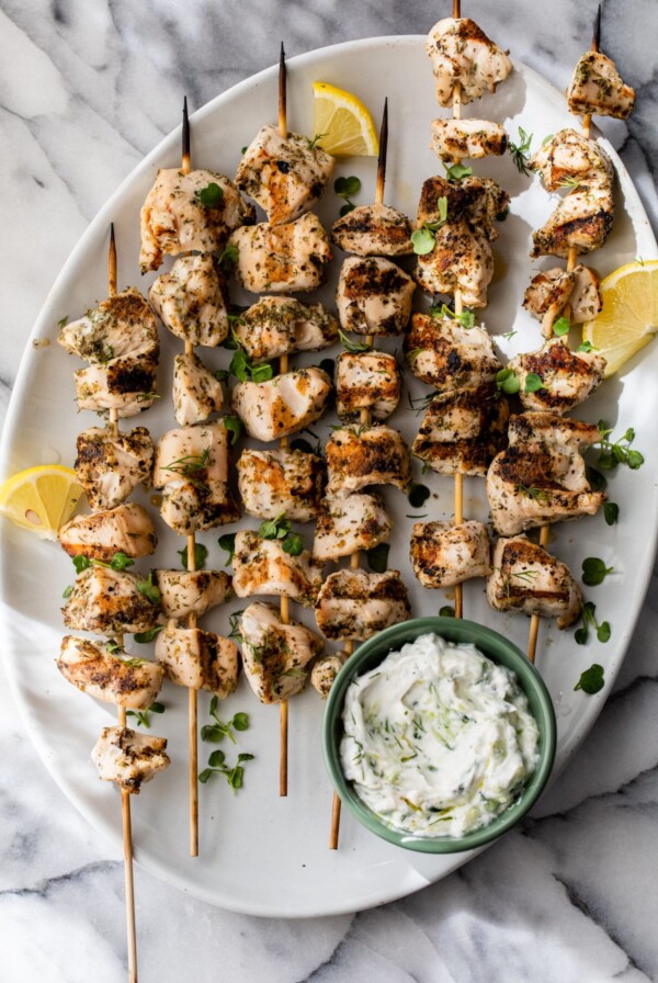 greek chicken skewers on a plate with tzatziki sauce on the side