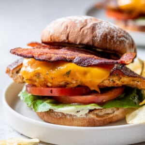 a Grilled Chicken Sandwich topped with bacon, melted cheese, tomatoes, and lettuce on a white plate.