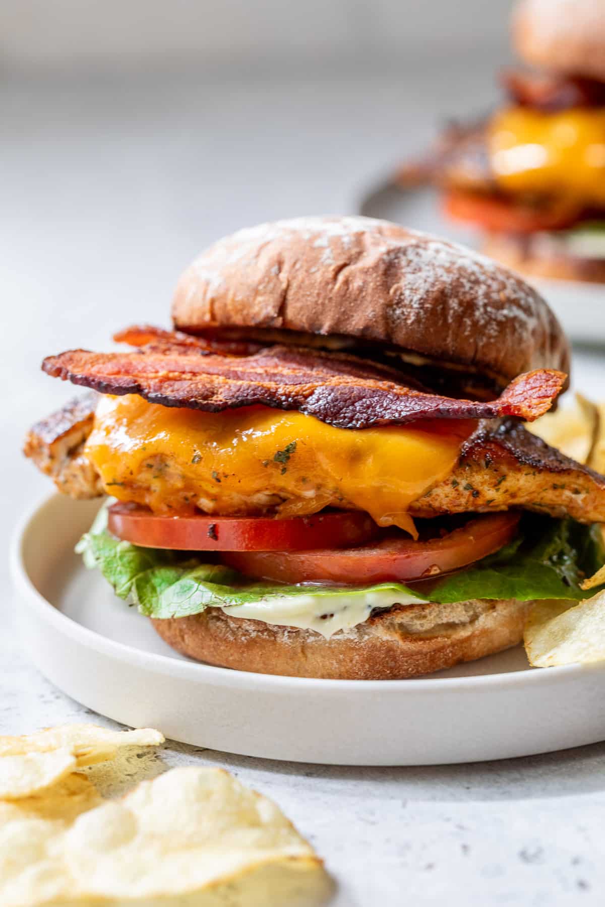 a Grilled Chicken Sandwich topped with bacon, melted cheese, tomatoes, and lettuce on a white plate.