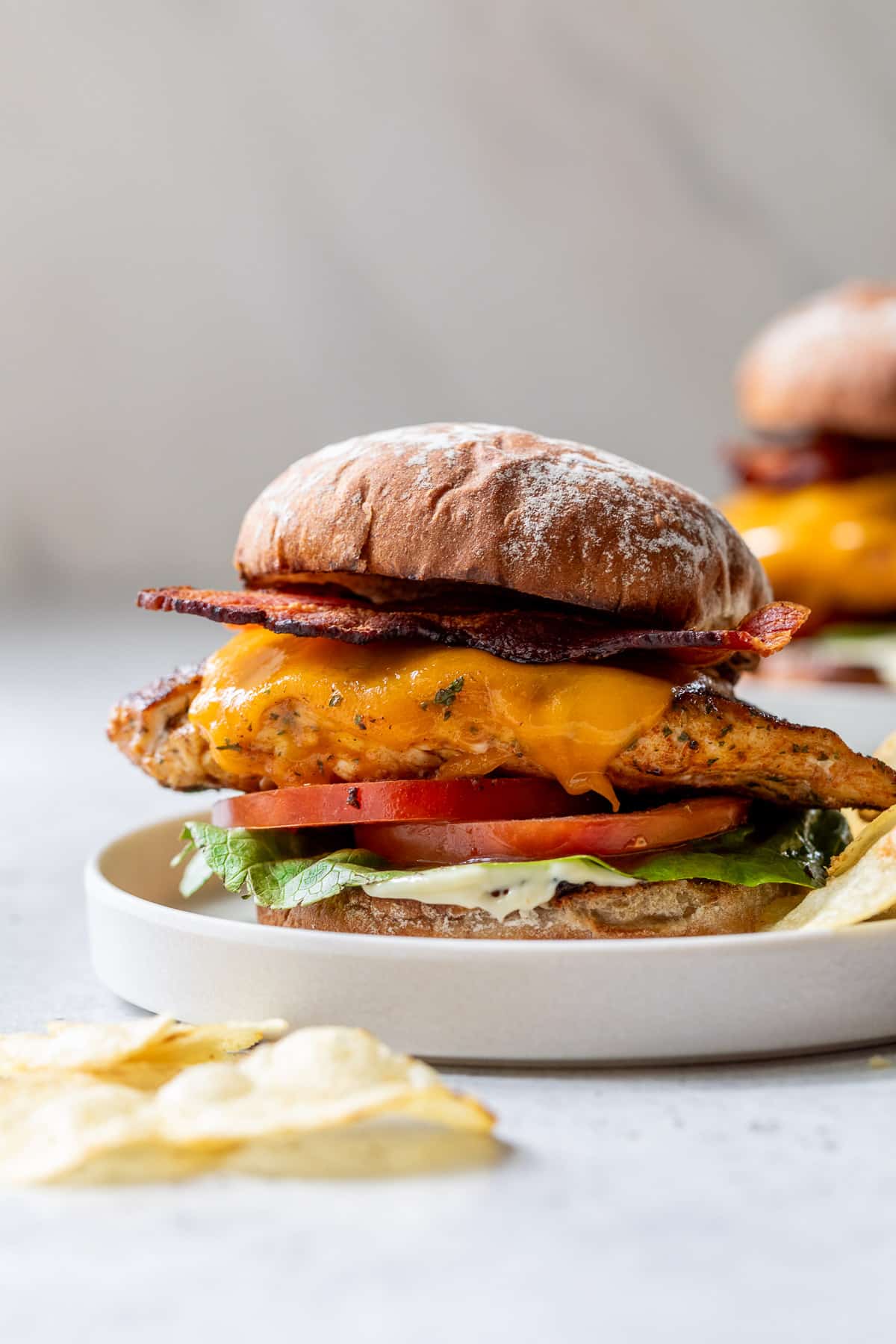 a Grilled Chicken Sandwich topped with bacon, melted cheese, tomatoes, and lettuce on a white plate.