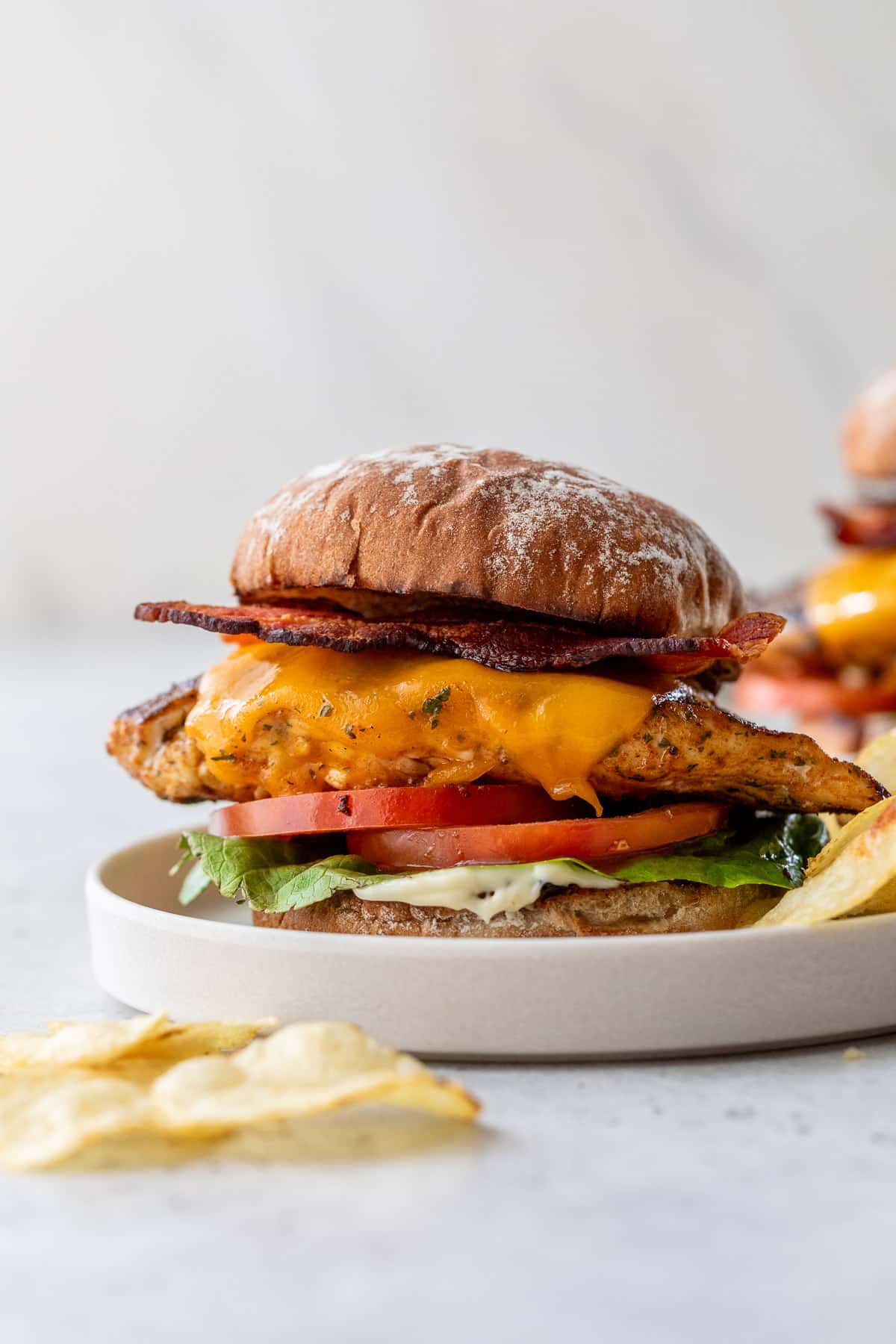 a Grilled Chicken Sandwich topped with bacon, melted cheese, tomatoes, and lettuce on a white plate.