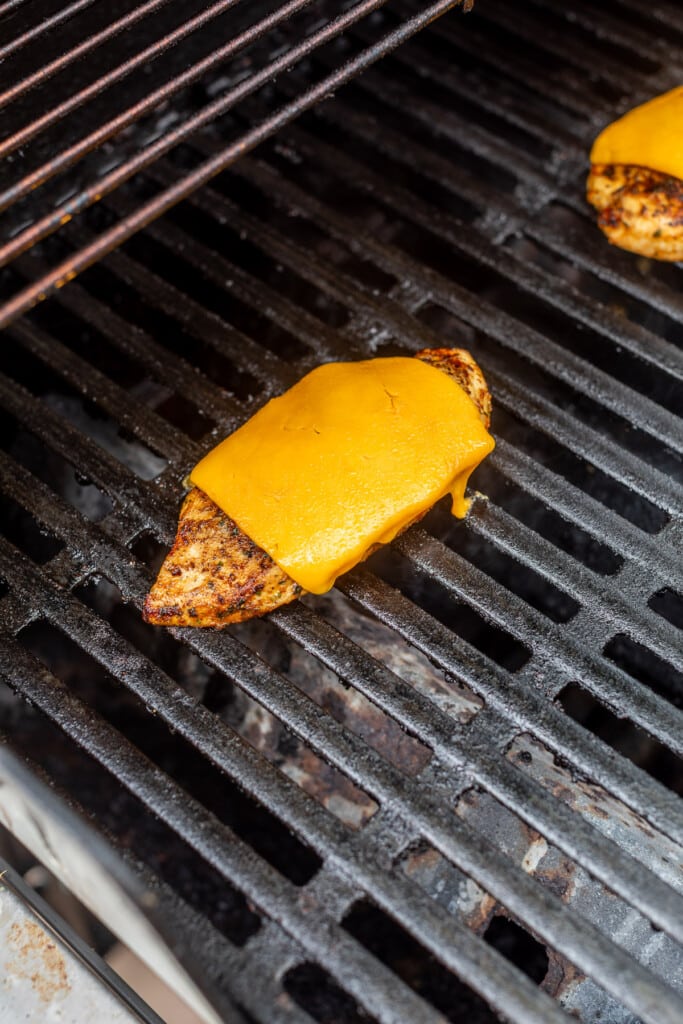a chicken breast topped with melted cheese on an outdoor grill.