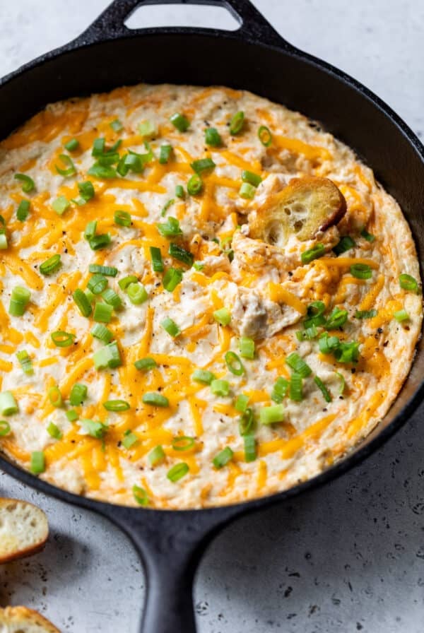dipping a baguette slice in hot crab dip in a large black skillet.