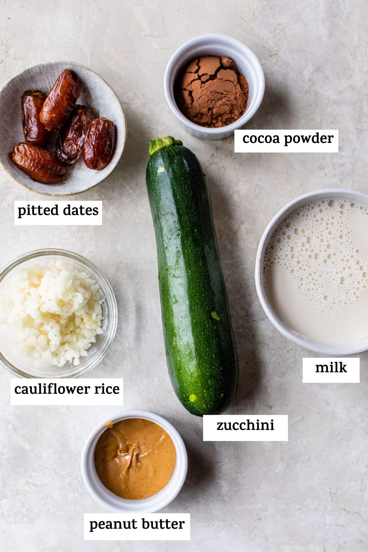 all ingredients for the smoothie displayed: pitted dates, cauliflower rice, peanut butter, zucchini, milk, and cocoa powder