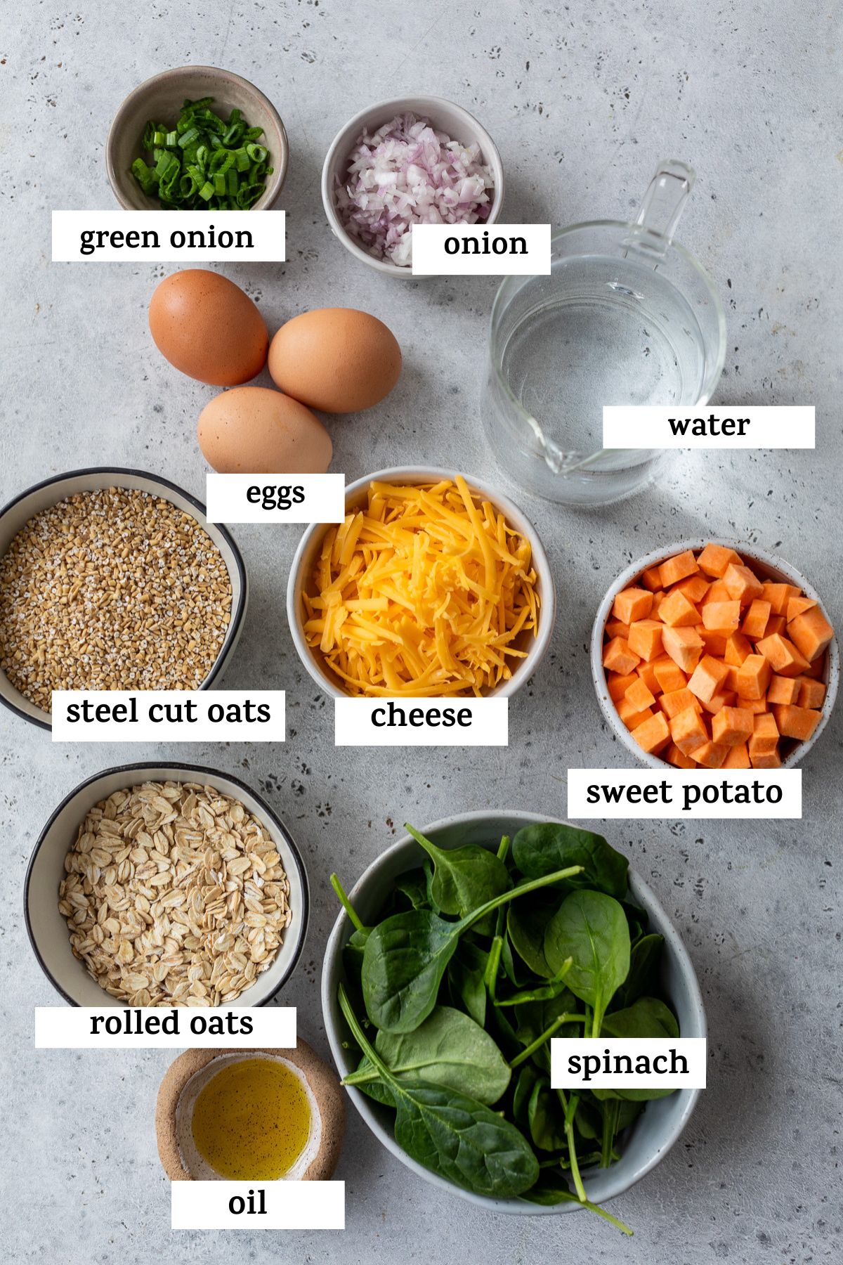 all ingredients listed out on a table; green onion, onion, eggs, water, steel cut oats, cheese, sweet potato, rolled oats, oil, and spinach