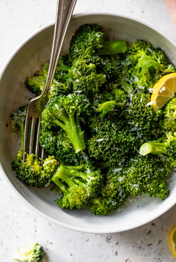 a large bowl of cooked broccoli sprinkled with grated cheese