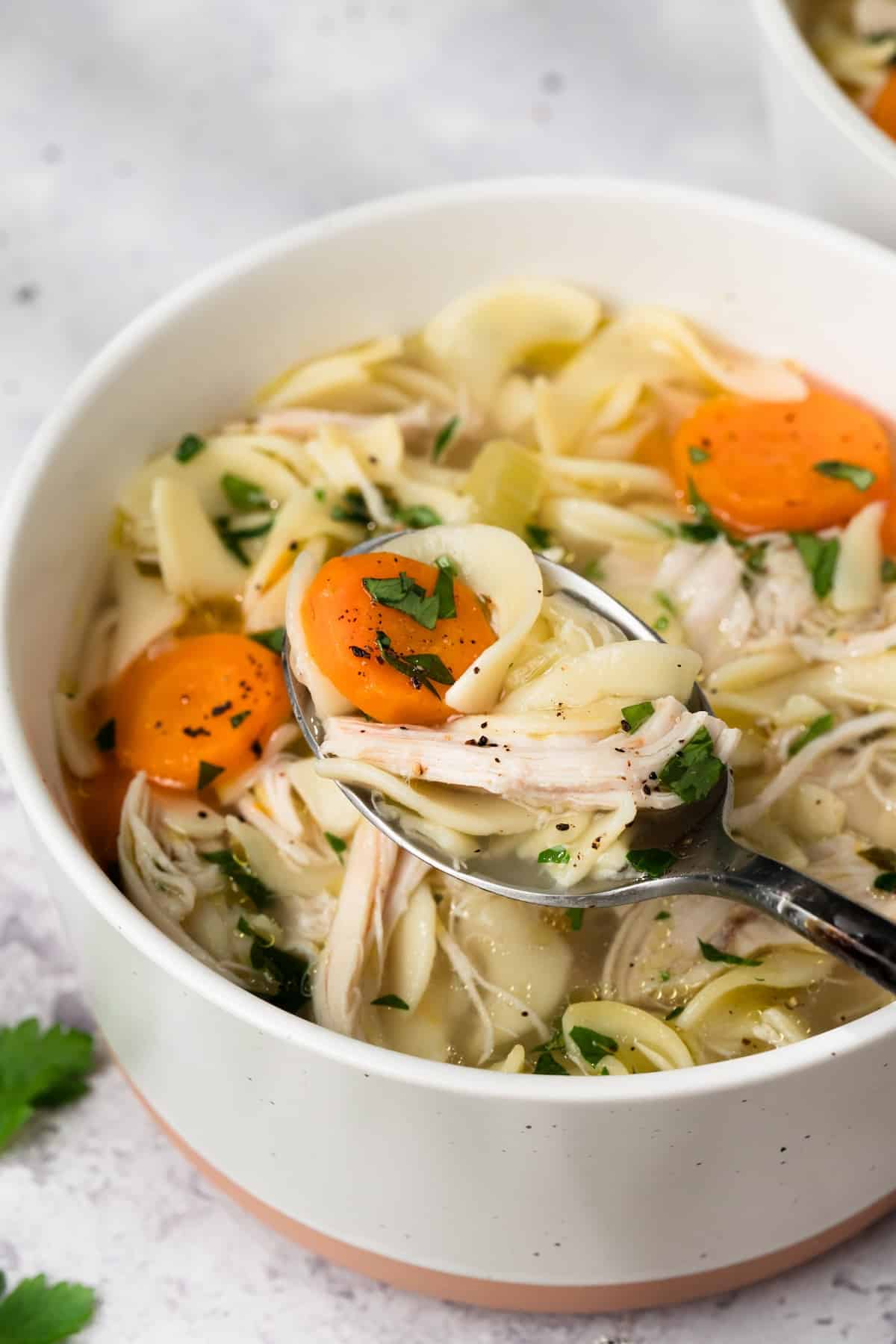close up on a spoonful of instant pot chicken noodle soup being lifted from a bowl.