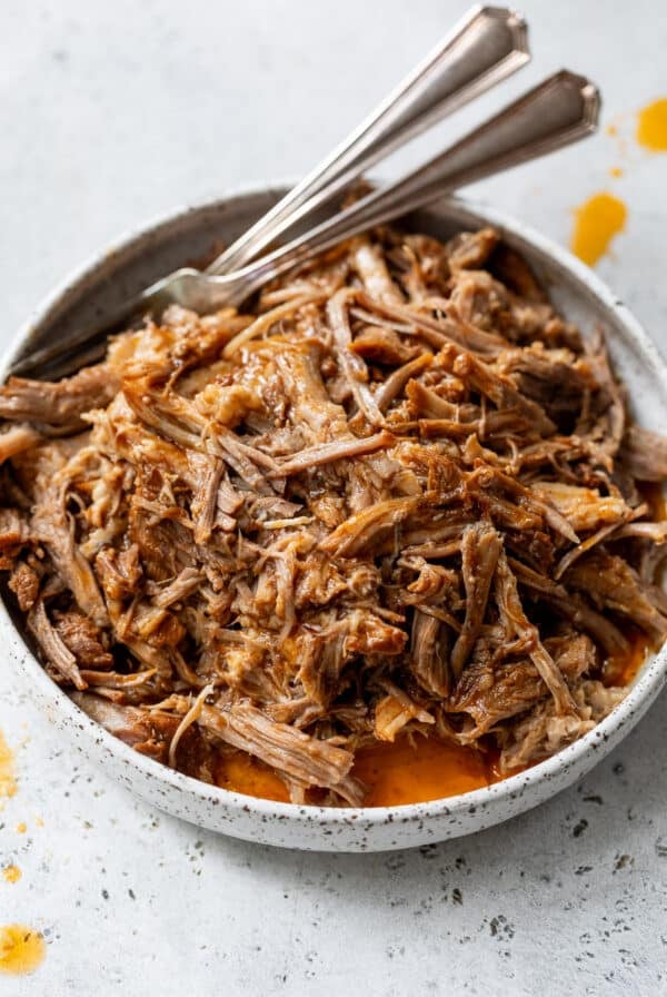 a bowl of Instant Pot Pulled Pork with 2 forks on the side.
