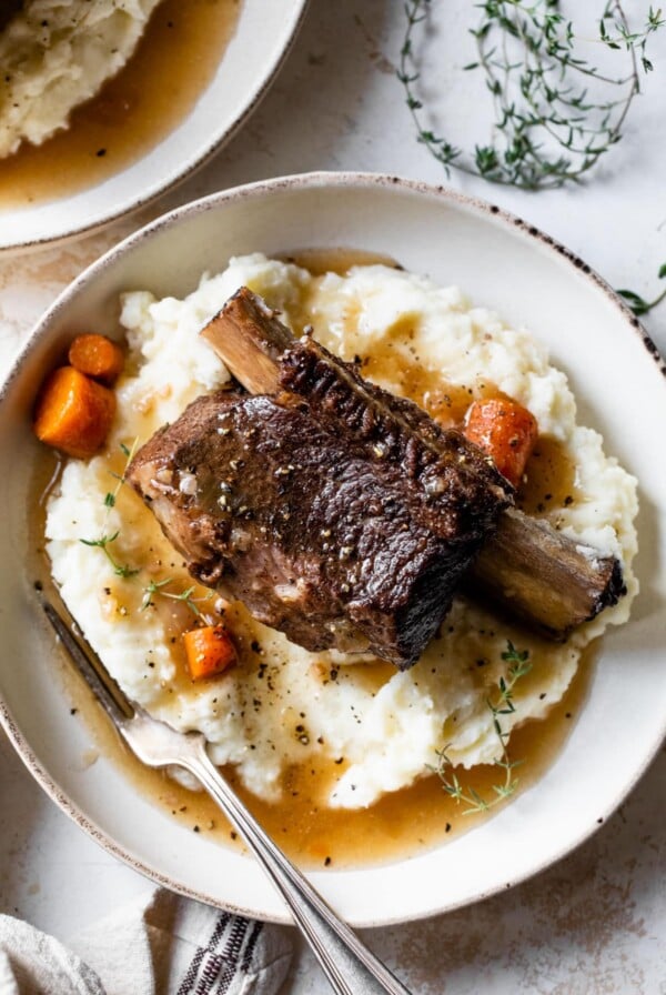overview of short ribs on top of mashed potatoes and gravy on a plate with a fork